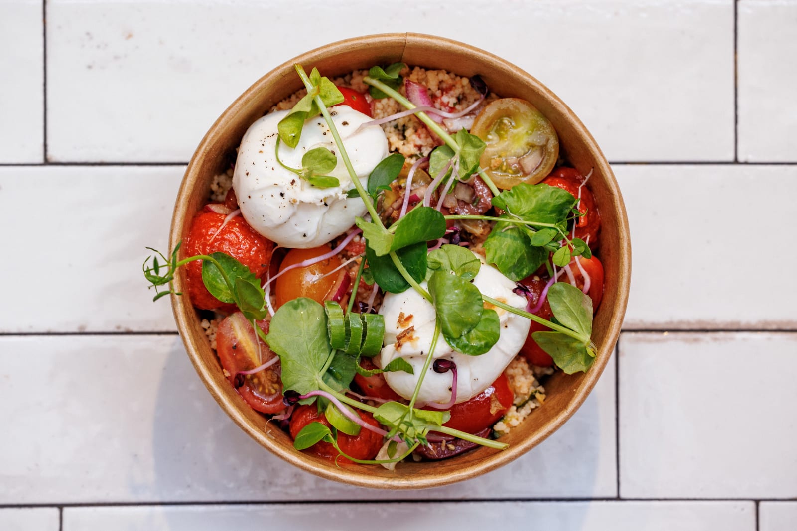 Kartonnen bowl met burrata, tomaten en scheuten op witte tegels