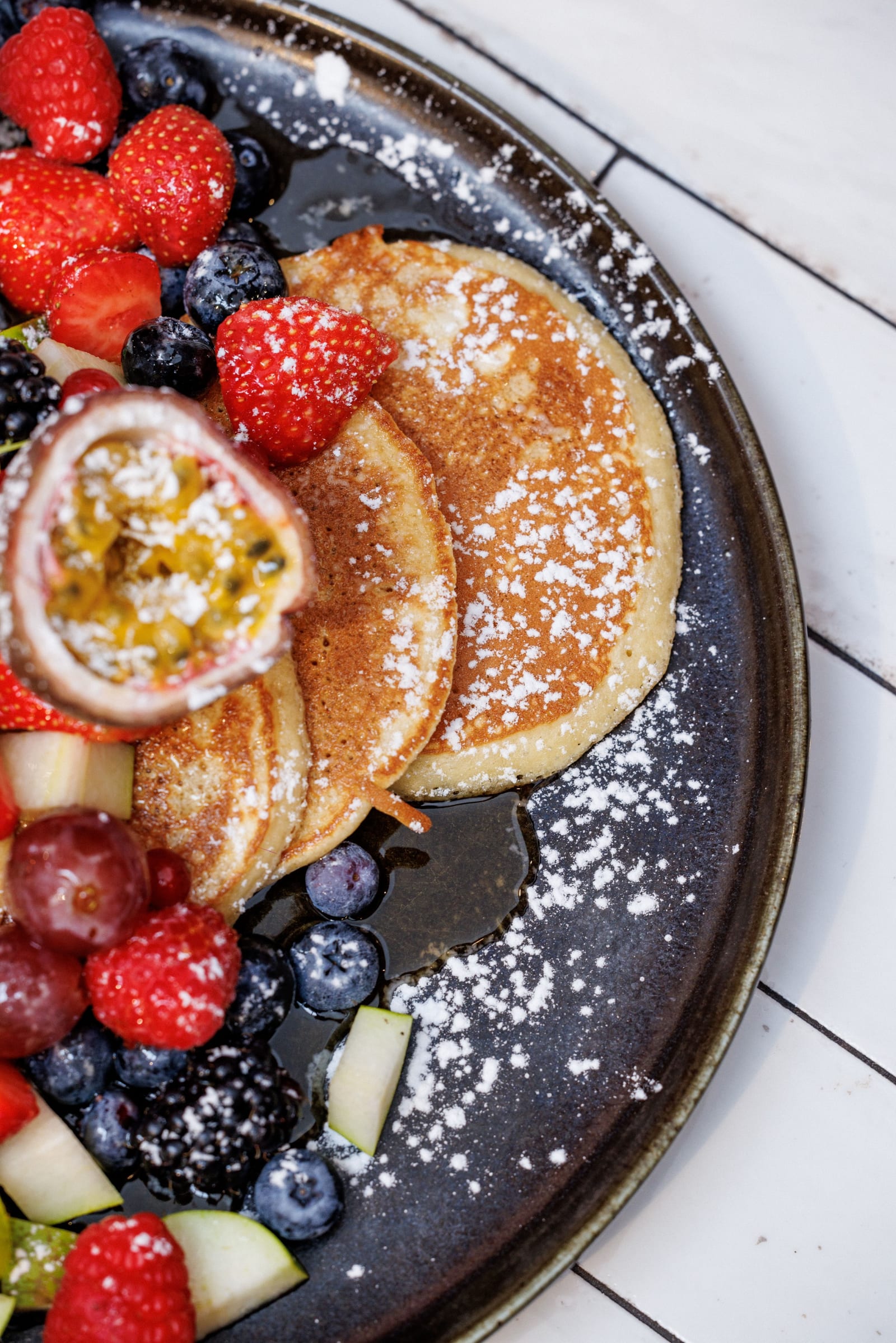 Pancakes met poedersuiker en vers fruit op een donker bord