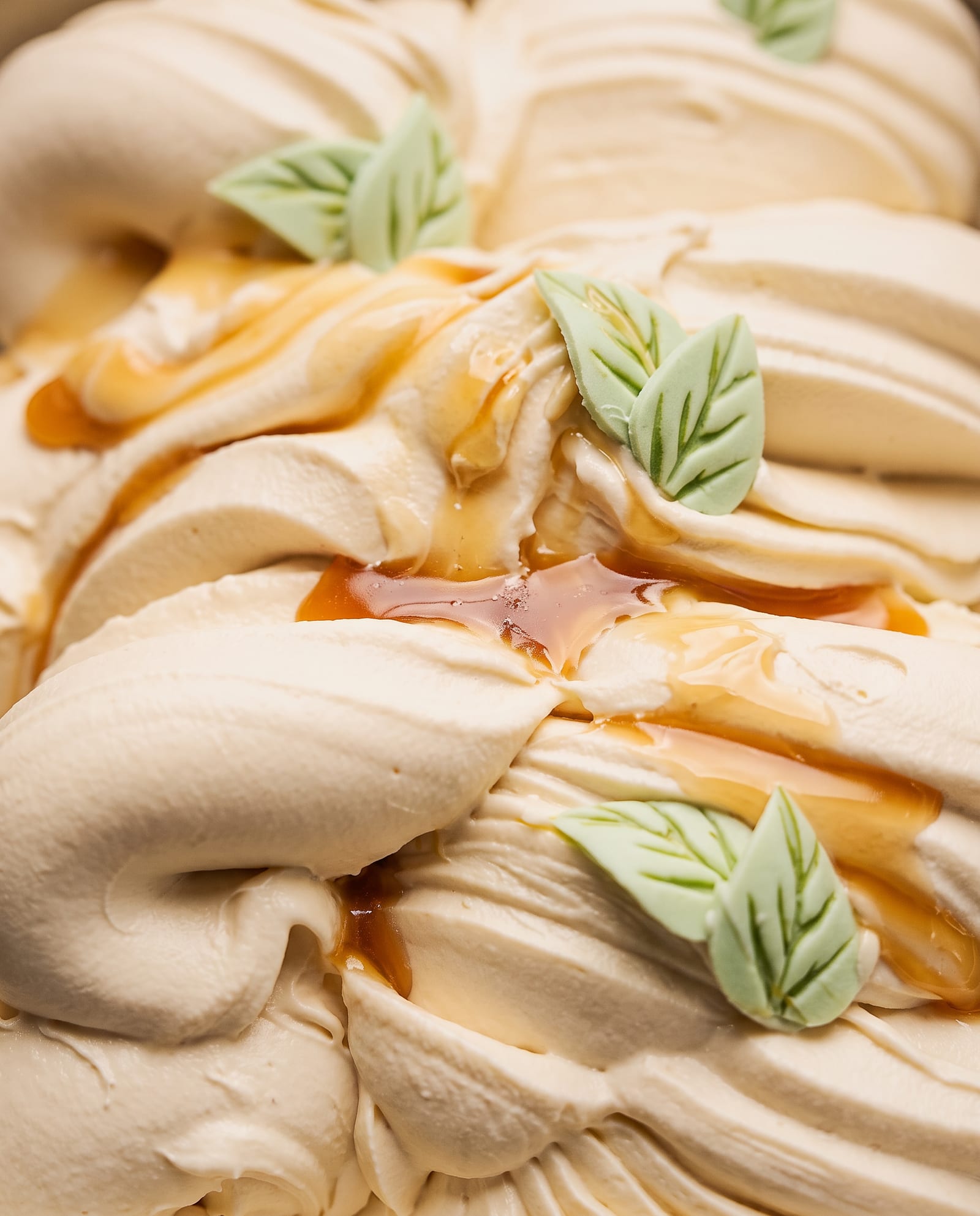 Close-up: crèmekleurig caramelijs met slierten caramelsaus en lichtgroene suikerblaadjes als decoratie