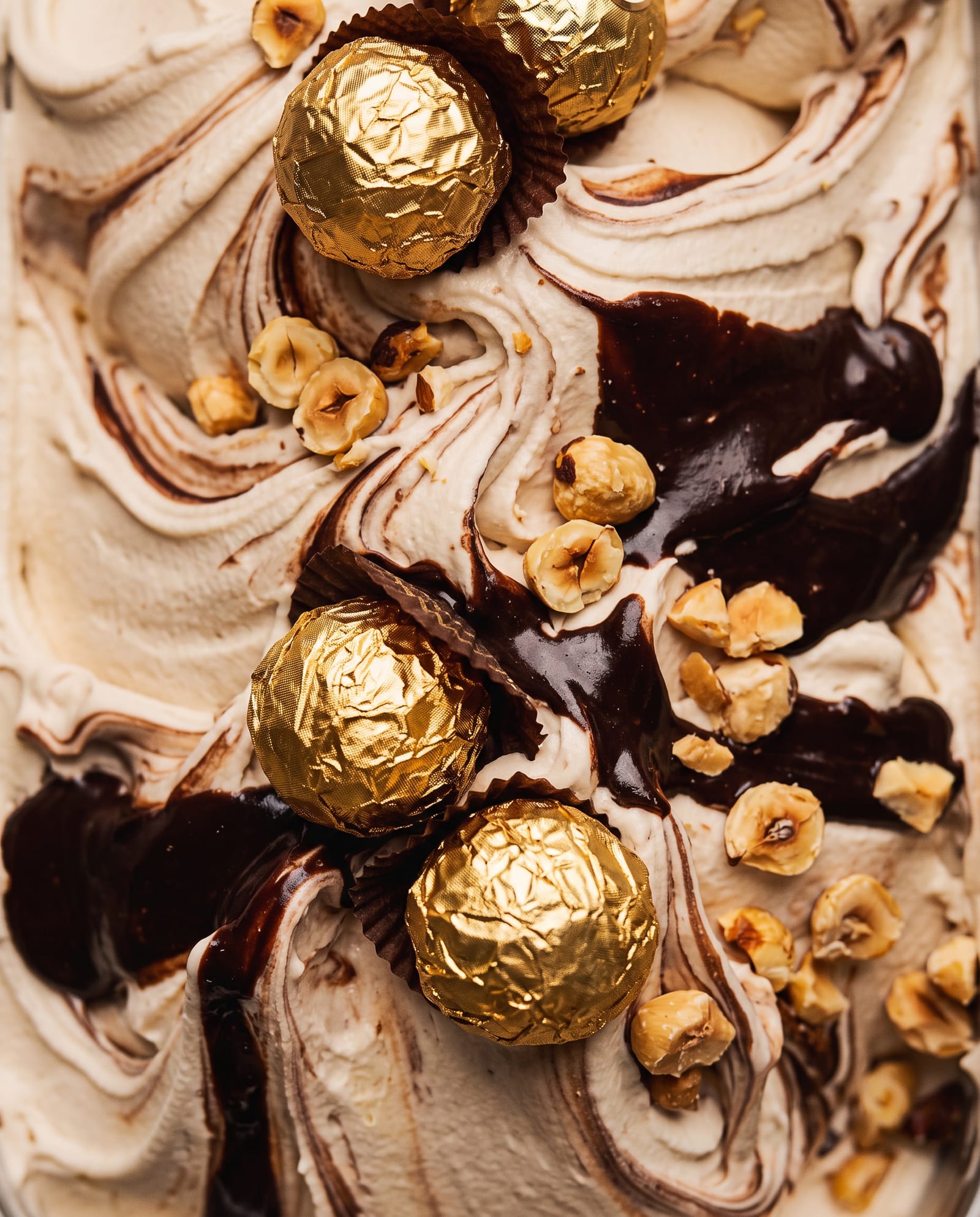 Close-up: licht hazelnootijs met een chocoladeswirl, hazelnoten en pralines in goudfolie