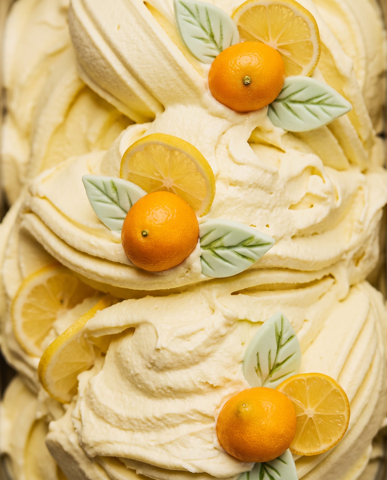 Close-up: lichtgele limoncellosorbet met citroenschijfjes, kleine oranje citrusvruchtjes en lichtgroene suikerblaadjes