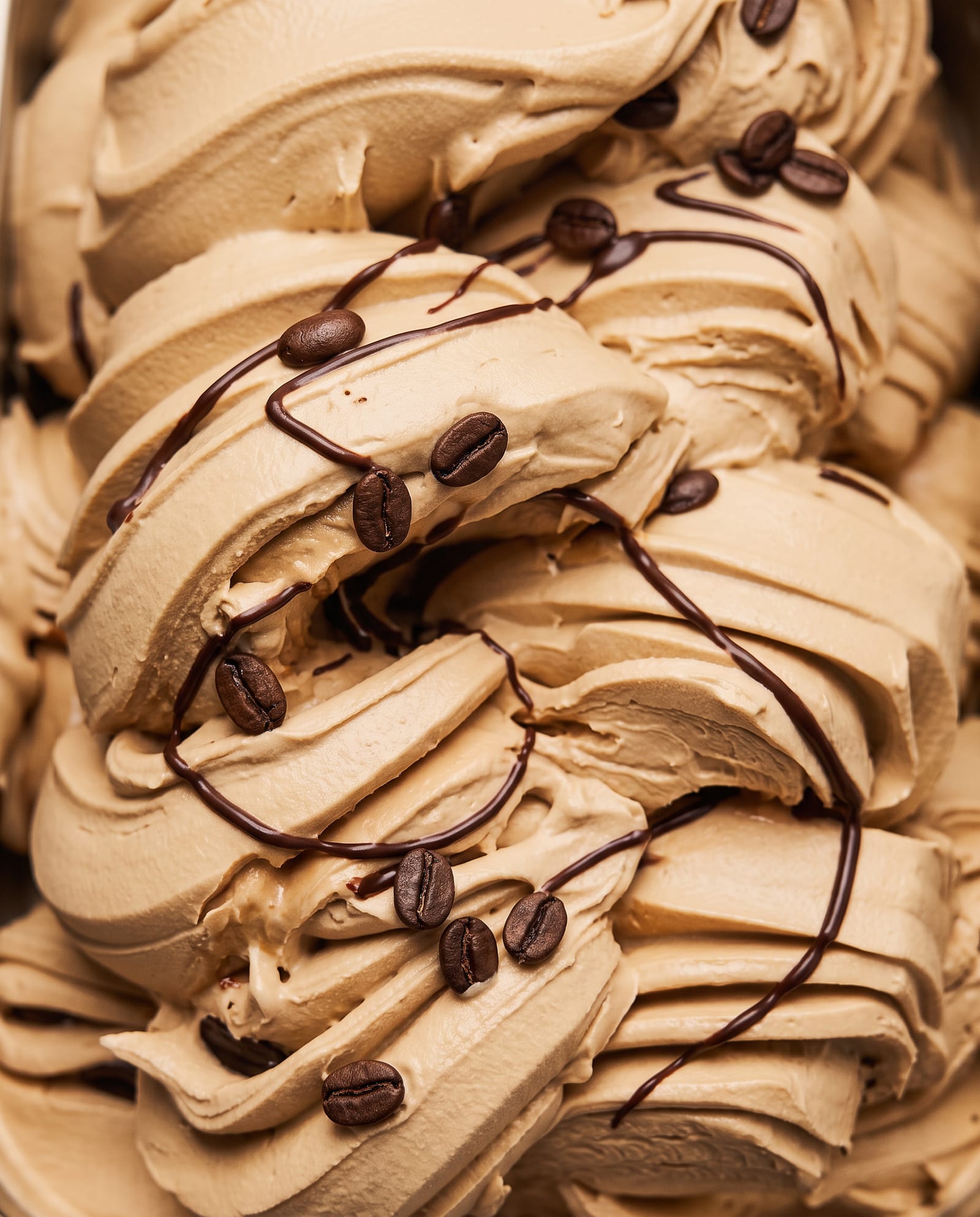 Close-up: lichtbruin koffie-ijs in swirls met koffiebonen en dunne strepen chocoladesaus